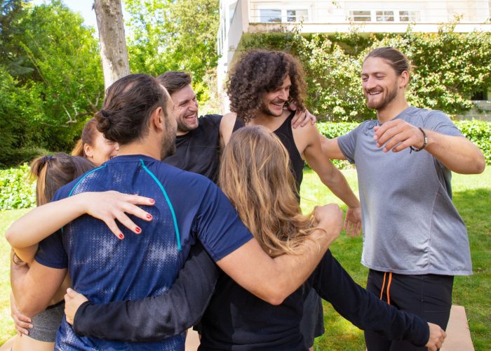 Cheerful young people hugging outdoor. Smiling young men and women in sportswear gathering together in park for yoga practice. Yoga concept